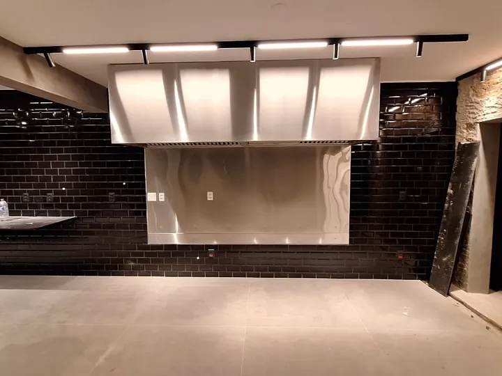 Coifa Box profissional em aço inox instalada sobre parrilla em espaço gourmet