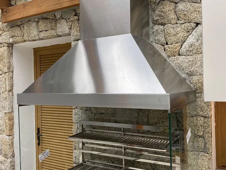 Coifa piramidal de parede em aço inox instalada sobre churrasqueira em área gourmet