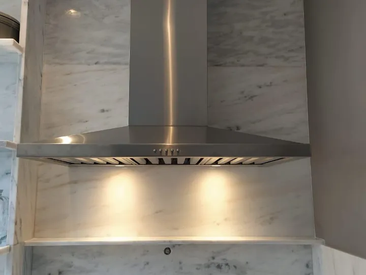 Coifa piramidal de parede com iluminação instalada sobre cooktop em cozinha