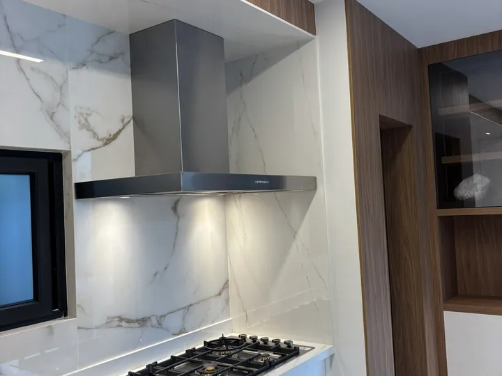 Coifa Slim de parede em aço inox instalada sobre cooktop em cozinha planejada