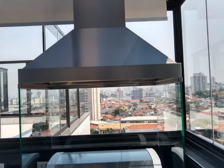 Coifa piramidal para churrasqueira instalada sobre ilha em varanda gourmet.